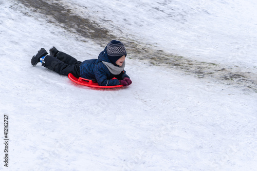 A little boy rides a sled from a winter slide.