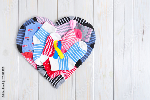 Heart formed by different striped and colored children's socks on a wooden background. In the center there is a yellow and blue ribbon. World Down Syndrome Day concept.