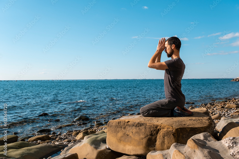 Attractive young man practicing yoga meditation and breathwork outdoors by the sea Attractive young man practicing yoga meditation and breathwork outdoors by the sea