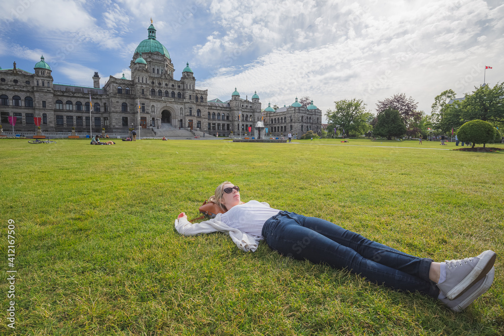 Fototapeta premium A young woman relaxes on the grass in front of the Legislative Assembly of British Columbia on a sunny summer day in Victoria, Canada.