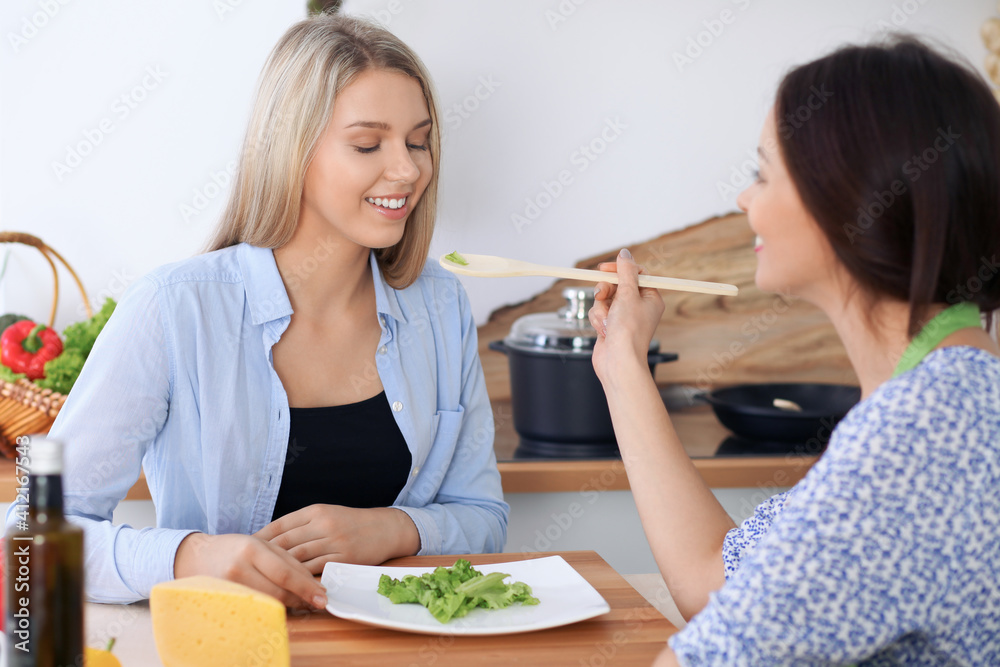 Two young happy women are cooking in the kitchen. Friends are having fun while preapering healthy and tasty meal Two young happy women are cooking in the kitchen. Friends are having fun while preapering healthy and tasty meal