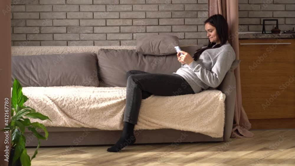 Relaxed young smiling woman using smartphone talking on the phone, make video call, recording vlog sitting on sofa. Millennial lady spending time at home with cell gadget technology Relaxed young smiling woman using smartphone talking on the phone, make video call, recording vlog sitting on sofa. Millennial lady spending time at home with cell gadget technology