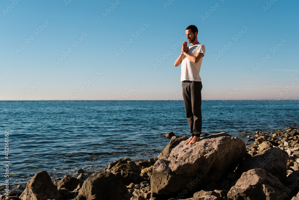 Attractive young man practicing yoga meditation and breathwork outdoors by the sea