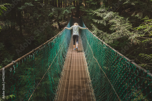 Bild auf Leinwand A young woman crosses a rainforest suspension bridge on the Juan de Fuca trail on the way to Mystic Beach on Vancouver Island, British Columbia in the pacific northwest Canada
