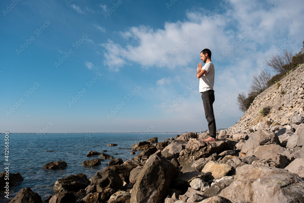 Obraz premium Attractive young man practicing yoga meditation and breathwork outdoors by the sea