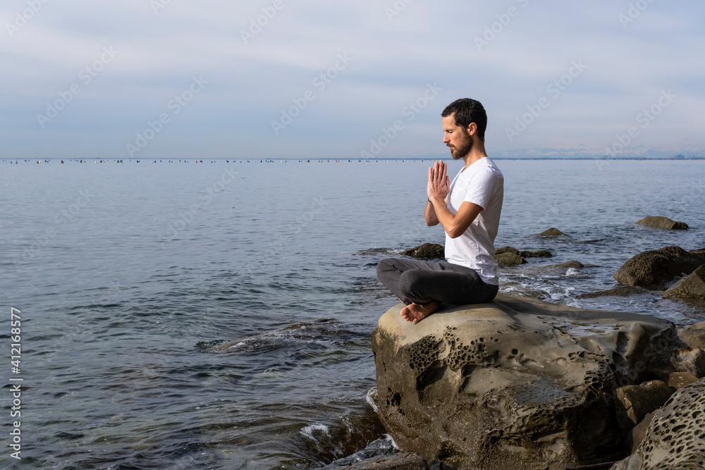 Attractive young man practicing yoga meditation and breathwork outdoors by the sea Attractive young man practicing yoga meditation and breathwork outdoors by the sea