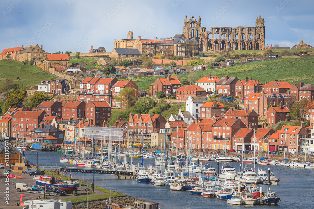 Rooftop cityscape view of Whitby townscape, River Esk Harbour, Humber estuary, and historical landmark Whitby Abbey on a sunny afternoon in North Yorkshire, England.
