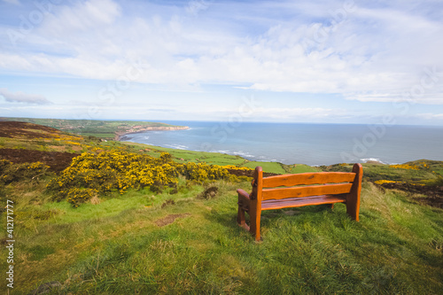 An empty park bench taking in cliffs and seaside landscape views at Ravenscar on the North Yorkshire Coast, part of the civil parish Staintondale in North York Moors National Park, England.