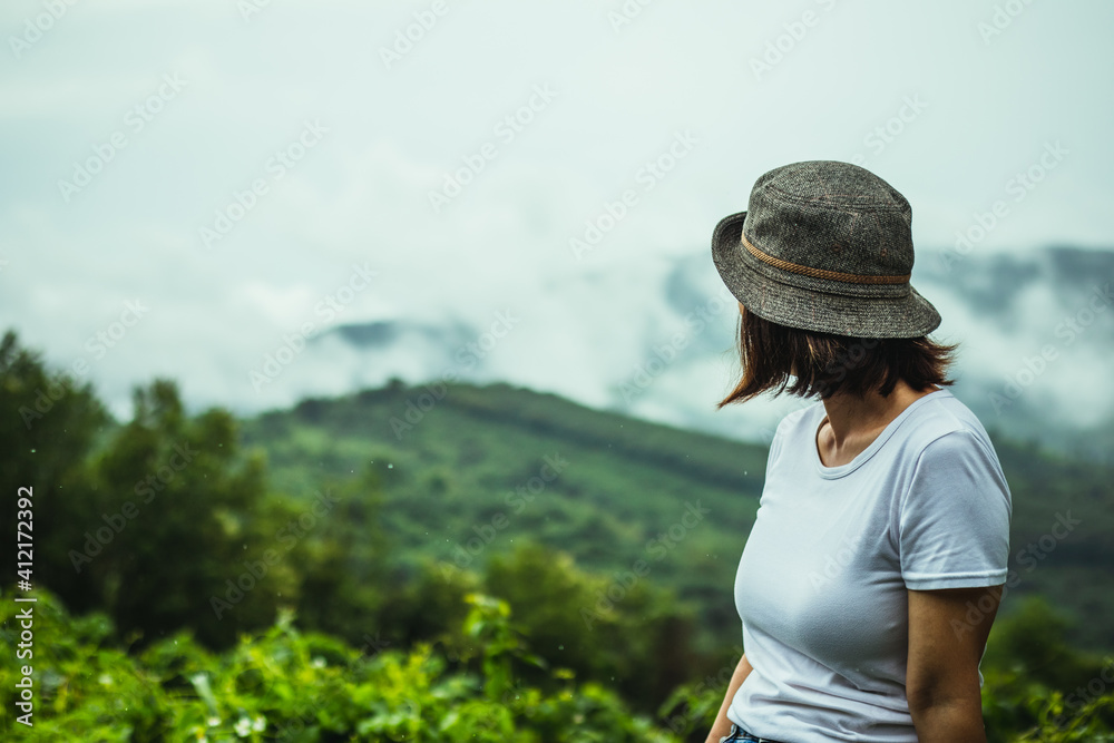 A woman standing on the top of a cliff in the mountains, the rainy season at sunset and enjoying the nature scenery.