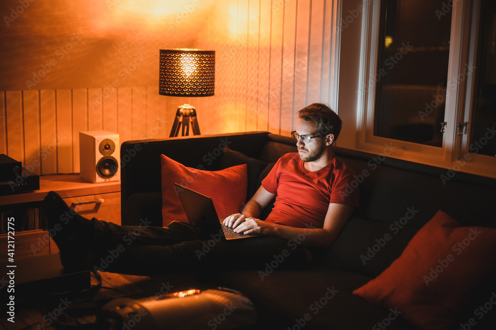 Portrait of attractive nerdy man is working late night on the computer in living room in home office Portrait of attractive nerdy man is working late night on the computer in living room in home office