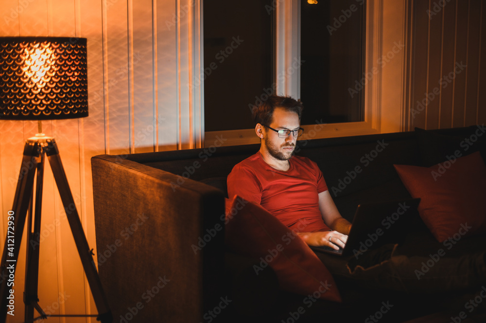 Portrait of attractive nerdy man is working late night on the computer in living room in home office