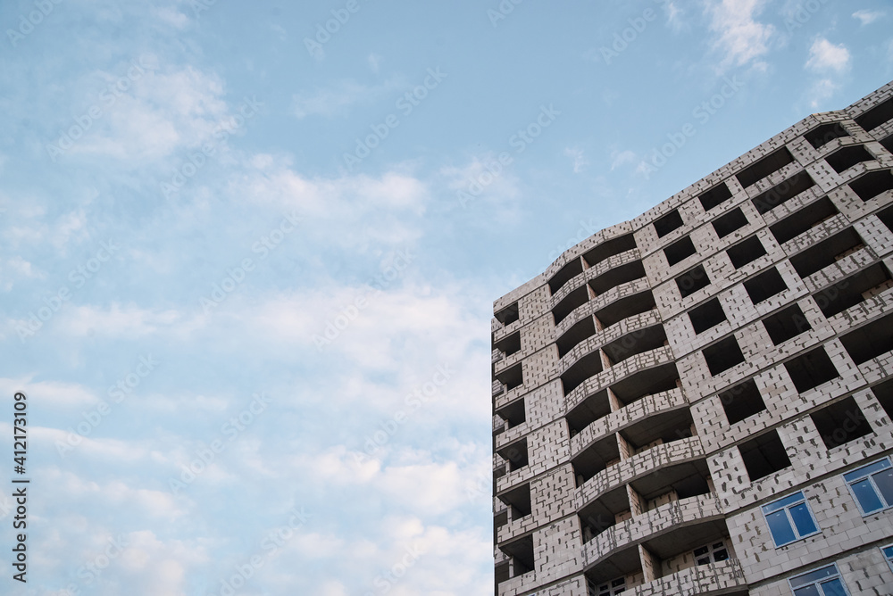 View from underneath on construction of grey concrete apartment building in front of blue sky with clouds. City dwelling. Urban architecture concept.