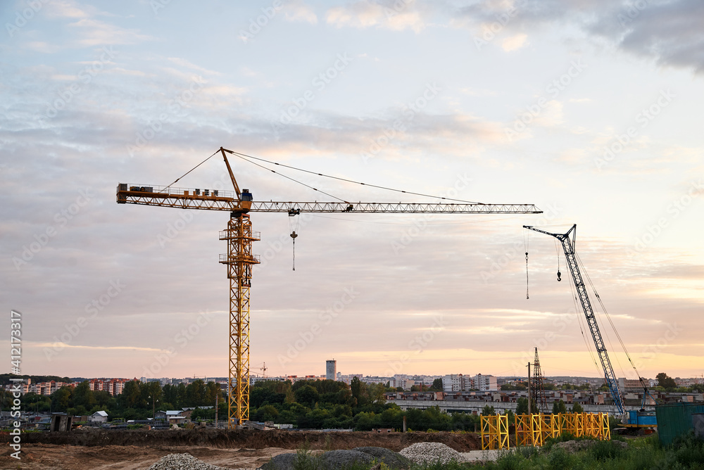 Beautiful city view at sunset. Industrial town landscape in the evening. Construction site with crane in front of blue pink cloudy sky.