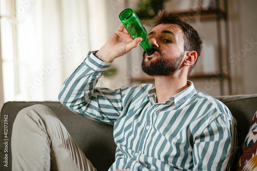 Young man at home. Man sitting in living room watching movie and drinking beer