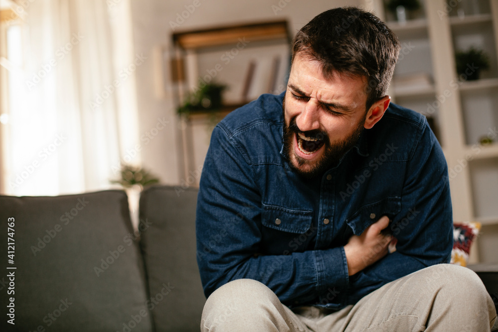 Sick man at home. Young man sitting on sofa having fever