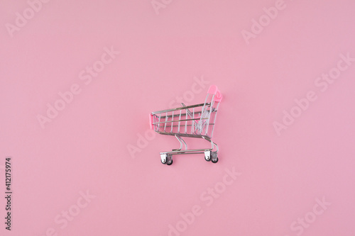 Empty mini pink shopping cart or trolley shopping on pink background. Shopping in supermarket or store.