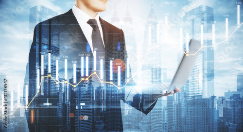 Business analytics concept with businessman following the process by laptop at city background and digital screen with infographic column diagram. Double exposure.