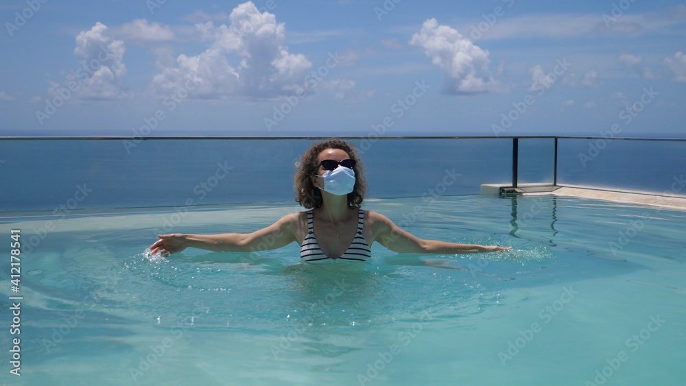 Travelling during covid-19 pandemic. Caucasian woman wearing face mask chilling in an infinity swimming pool 