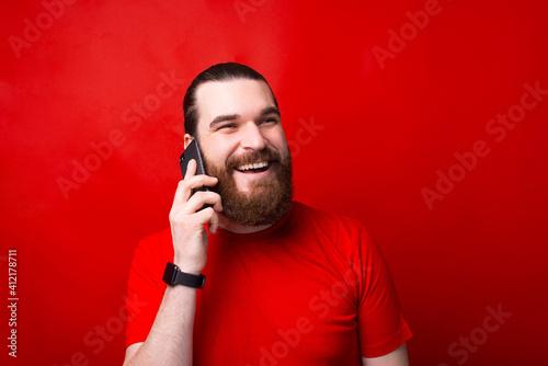 Portrait of happy bearded man talking on smartphone over red background. © Vulp
