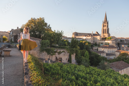 Fototapeta A young blonde tourist enjoying her holiday and vineyard view of the Monolithic Church and village of Saint-Emilion in Bordeaux wine country on a sunny summer day