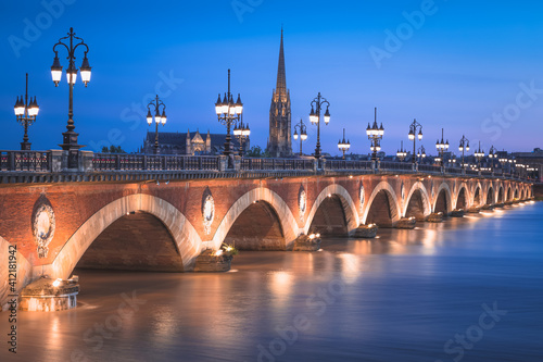 The historic Pont de Perre illuminated at night over the River Gardonne in Bordeaux, France with Bordeaux Cathedral in the background. photo