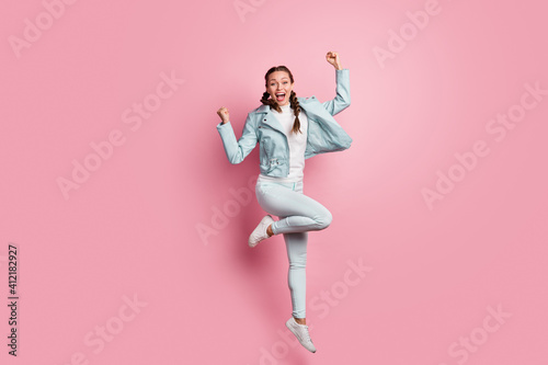 Full length photo portrait of celebrating woman with raised fists jumping up isolated on pastel pink colored background