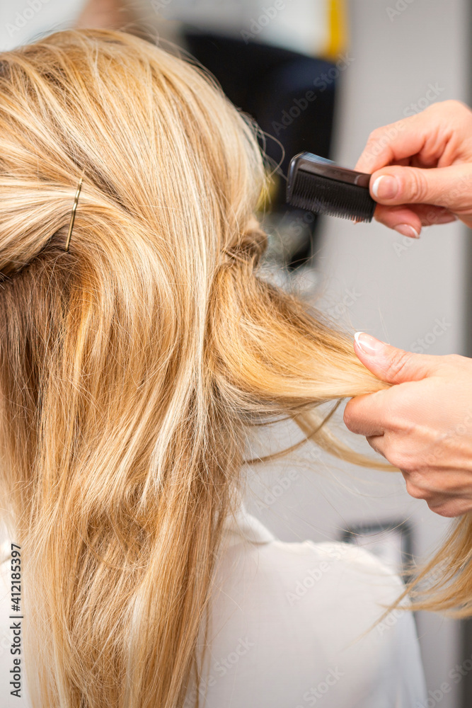 Fototapeta premium Rear View of a hairdresser combs blonde hair of the young woman in a beauty salon