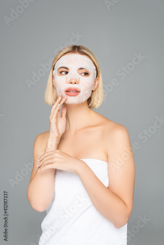Young woman in towel and sheet mask on face isolated on grey
