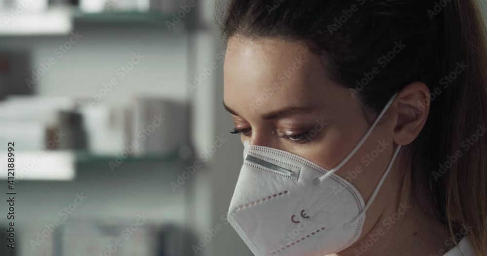Cinematic macro shot of female pharmacist consultant putting on protective N95 respirator mask and visor in pharmacy. Concept:covid-19, protection, coronavirus, safety, health care and medical workers