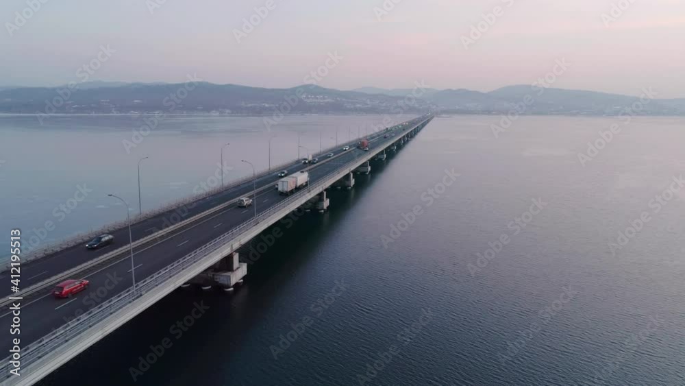 Aerial drone view of low-water bridge across the bay with moving car during the sunset. Active movement of transport cars vehicles in different directions. Aerial drone view of low-water bridge across the bay with moving car during the sunset. Active movement of transport cars vehicles in different directions.