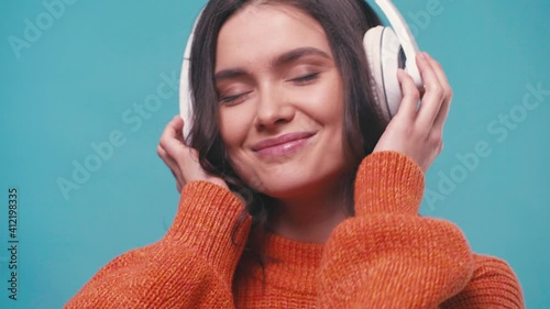 pleased woman in wireless headphones listening music isolated on blue