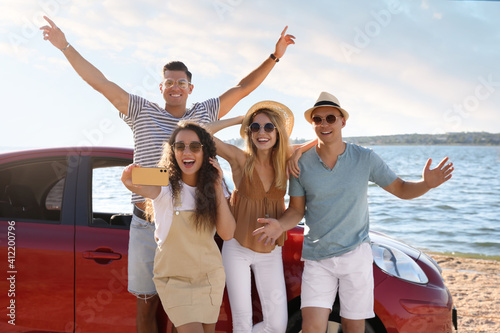 Happy friends taking selfie near car on beach. Summer trip