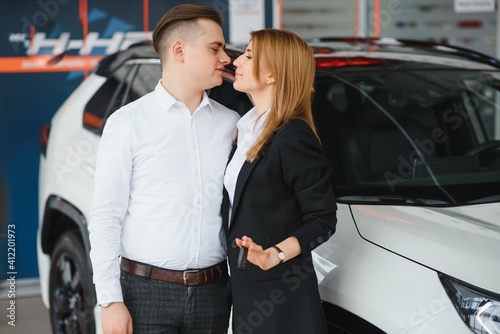 Visiting car dealership. Beautiful couple is holding a key of their new car and smiling, girl is kissing her husband in cheek © Serhii