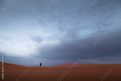 A distant figure exploring sand dunes desert landscape against a moody, dramatic sky at Erg Chebbi near the village of Merzouga, Morocco.