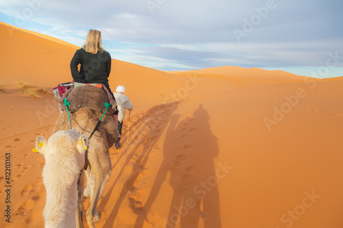 A young blonde female tourist on a camelback excursion along the desert sand dunes of Erg Chebbi near the village of Merzouga in southeastern Morocco.