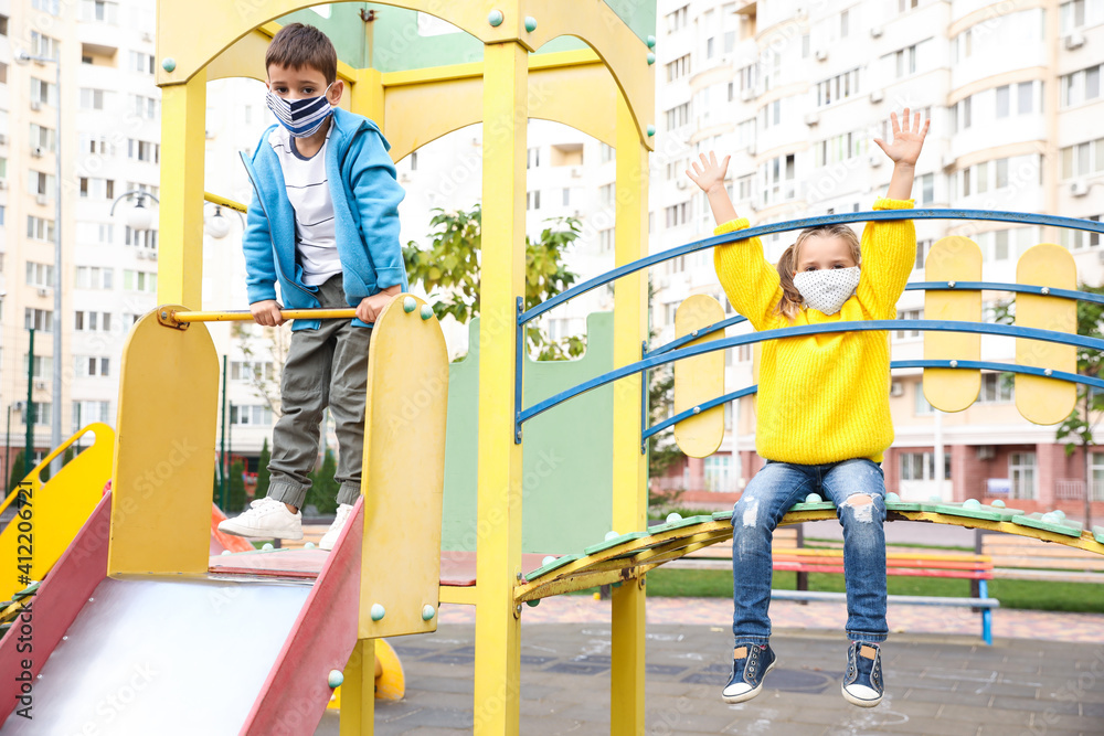 Little children with medical face masks on playground during covid-19 quarantine