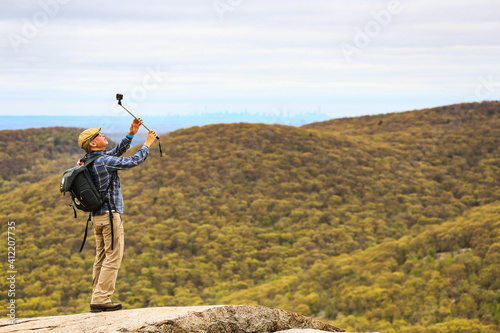 Man taking a photograph with a camera on a selfie stick with the Manhattan skyline in the background. Photo from Baer Mountain.