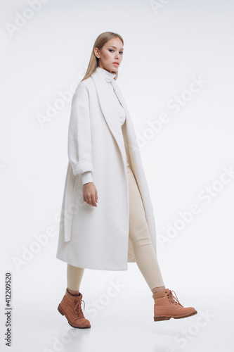 young fashionable beautiful girl in a trendy white coat posing on a white background