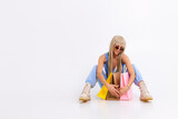 Fashion portrait of young happy blonde woman with long gorgeous straight hair with colorful shopping bags in the studio on a white background.