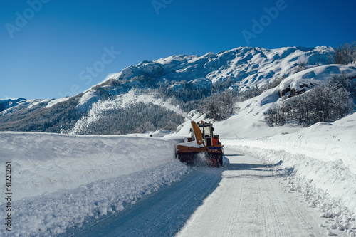A snowplow truck removing snow from a winding rural road on sunny winter day.