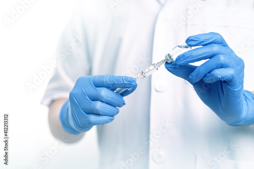 Man wearing white medical gown and blue gloves holding glass syringe and liquid vaccine bottle in white background. Disease medical and science concept. Fight against COVID-19 Coranavirus concept. photo