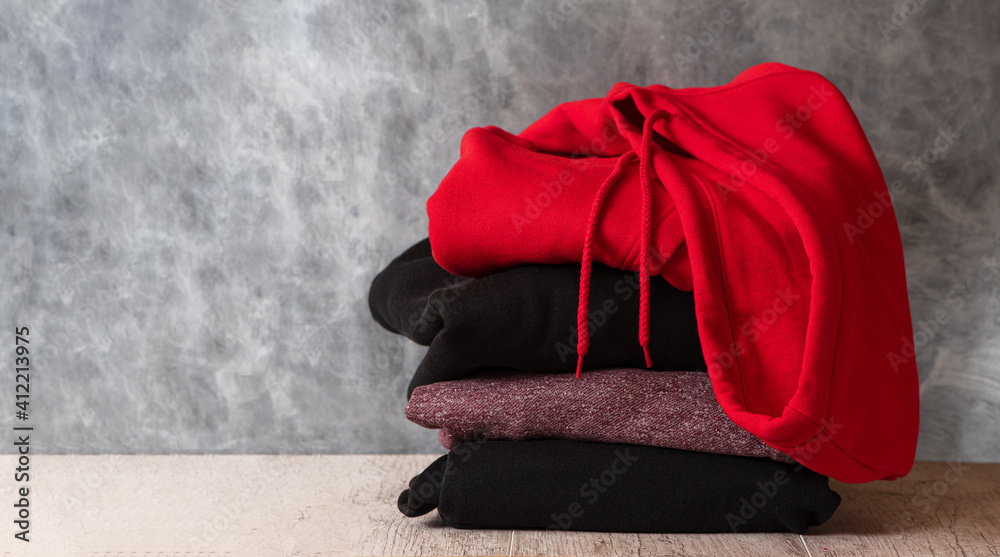 Stack of hooded sweatshirts and hoodie on gray background. Copy space.