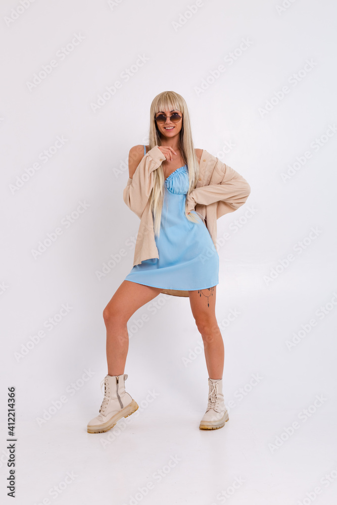 Fashionable portrait of a slender blonde with long chic hair in a light blue dress and a corduroy shirt in the studio on a white background Fashionable portrait of a slender blonde with long chic hair in a light blue dress and a corduroy shirt in the studio on a white background