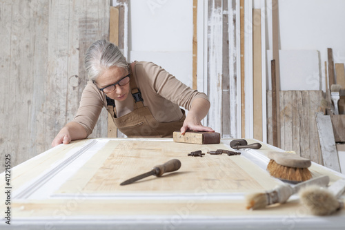 wood crafts, woman artisan carpenter works wood, sand an old door with sandpaper, with old handle tools in her workshop, restoration, diy and handmade works concept photo