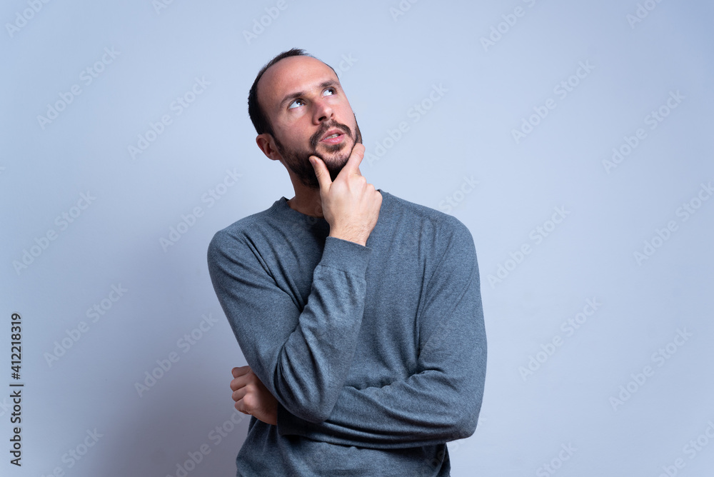 young man in studio thinking and looking toward the sky or the ceiling. pondering and imagining with hand on the chin. concentrated man in studio on white background. copy space