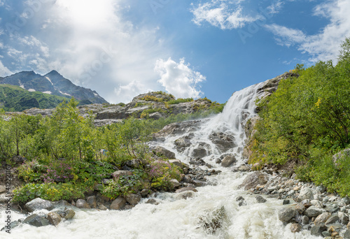 Beautiful waterfall. On a Sunny day the mountain stream flows among the forest . Panorama
