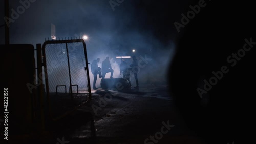 Wide shot of a group of men standing in the shadows in the night, dangerous criminals in smoke. Dangerous, urban scene.