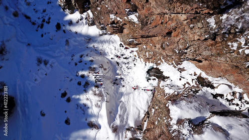 Freezing waterfall in the snowy mountains. View from the drone, from above. The rocks are covered with snow and ice. A small stream of water runs. The waterfall freezes. A group of people are resting photo
