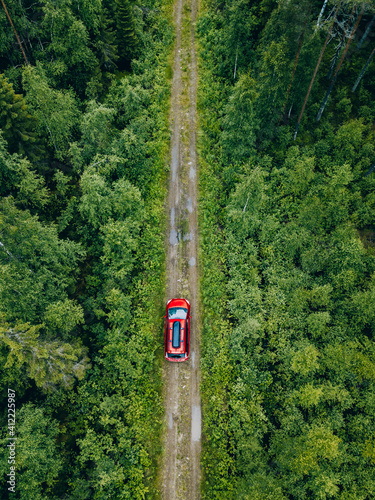 Aerial view of red car with a roof rack on a forest country road in Finland