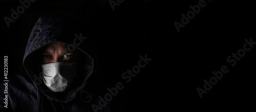 A man in a medical mask and a hood on a black background. Lockdown, social quarantine concept. Banner.